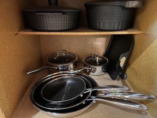 Inside cupboard view of several new frying pans, pots with lids