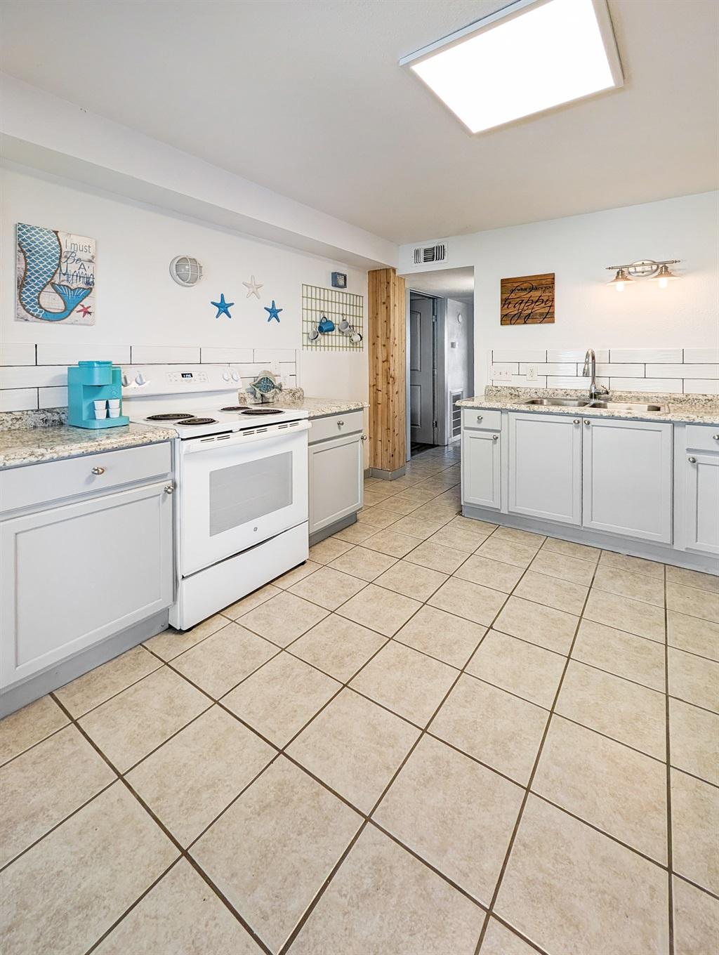 Spacious kitchen with white cabinets, white stove, granite countertops, tile flooring, and coastal wall decor accents.