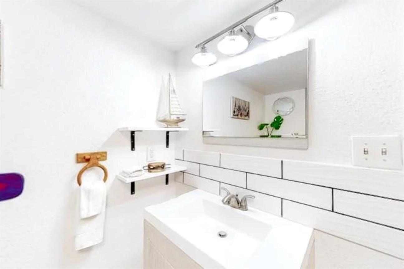 Bathroom vanity with a white sink, large mirror, overhead lighting, subway tile backsplash, and small shelves with decorative items.