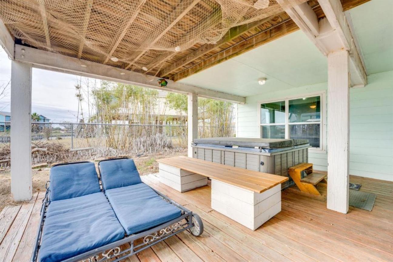 Covered patio with lounge chairs, a hot tub, bench seating, and wooden decking, surrounded by outdoor greenery.