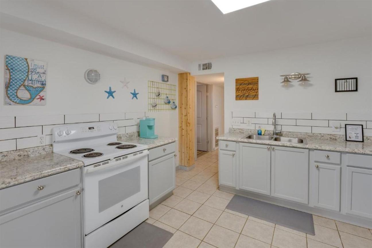 Large kitchen with white cabinets, white stove, granite countertops, tile flooring, and decorative coastal wall accents with stars and artwork.