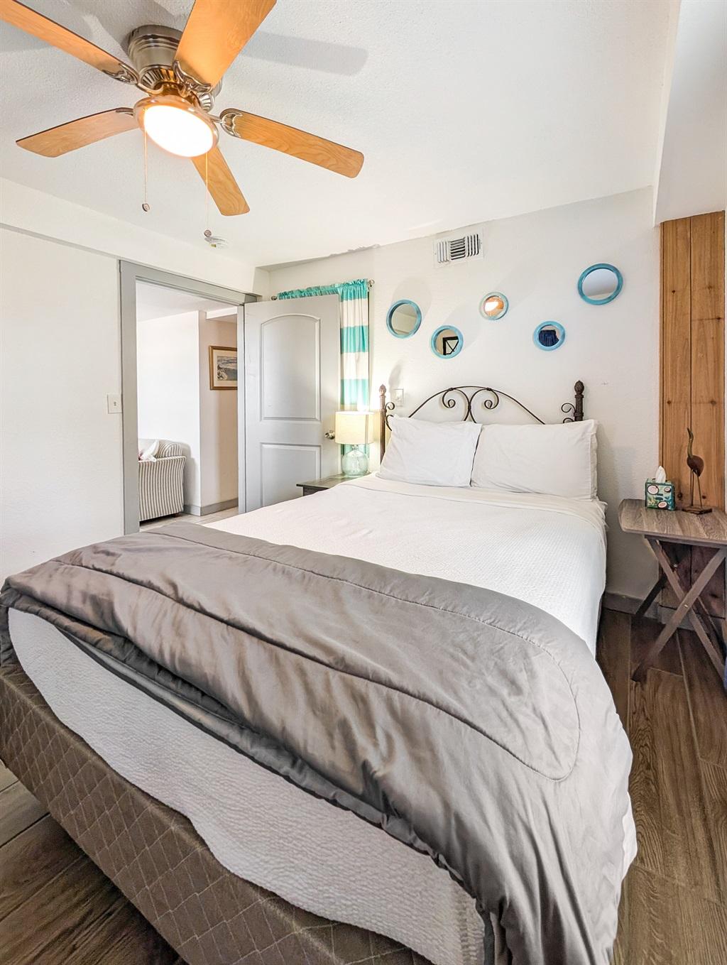 Bedroom with a bed featuring white and gray bedding, decorative wall accents above the headboard, bedside tables with lamps, wood-look flooring, and a ceiling fan overhead.