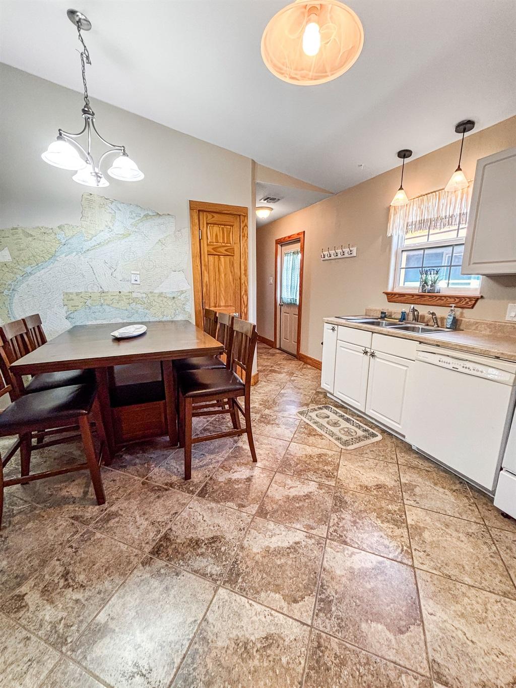 Dining space with a wooden table and chairs, white kitchen cabinets, sink under a window, and tile flooring with warm lighting.