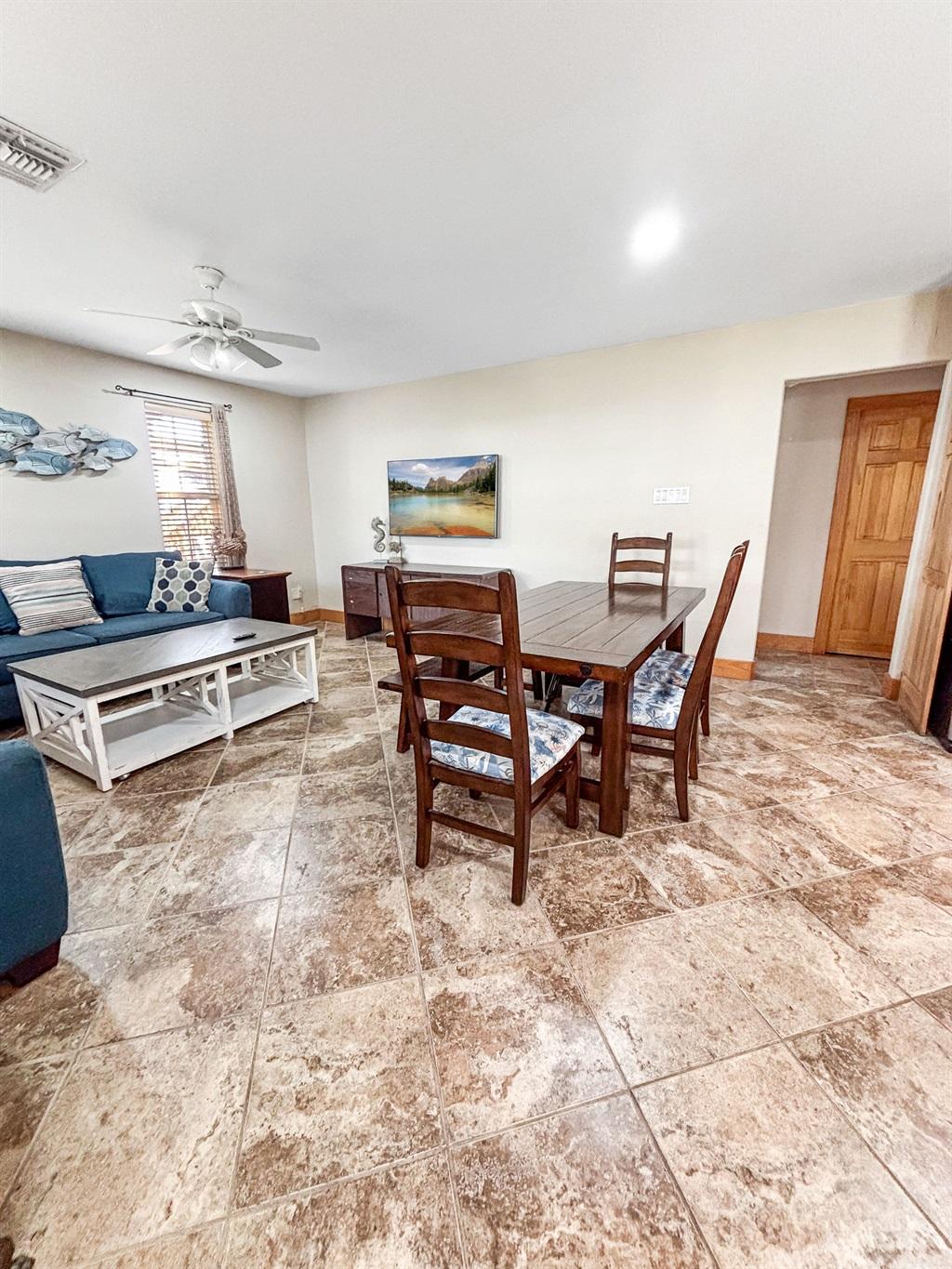 Dining area with a wooden table and four chairs on tile flooring, connected to a living room with a blue sofa and coffee table.