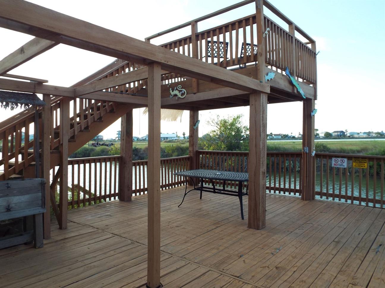Large wooden deck with stairs leading to an upper viewing platform, table for outdoor dining, and views of the water and surrounding landscape.