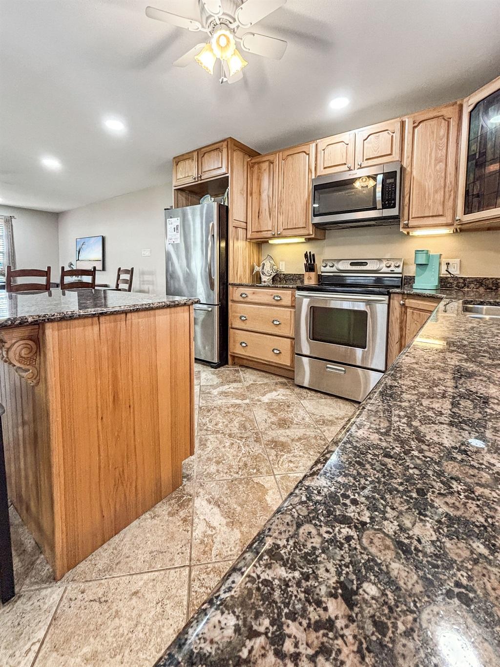 Kitchen with wood cabinets, granite countertops, stainless steel oven and refrigerator, and an island with bar seating on tile flooring.