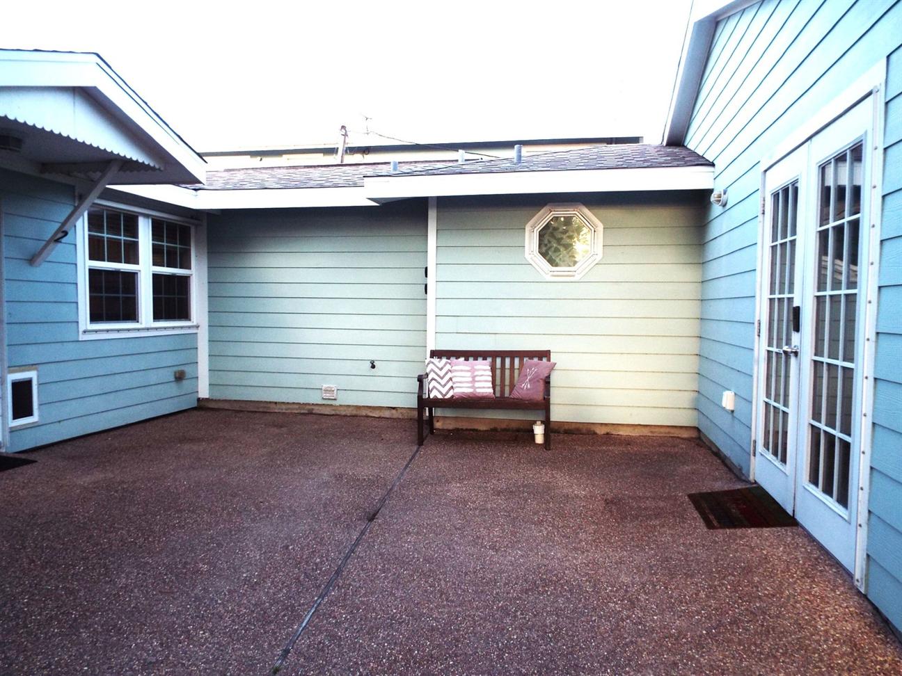 Enclosed outdoor patio with light blue siding, a bench with pillows, an octagonal window, and French doors leading inside