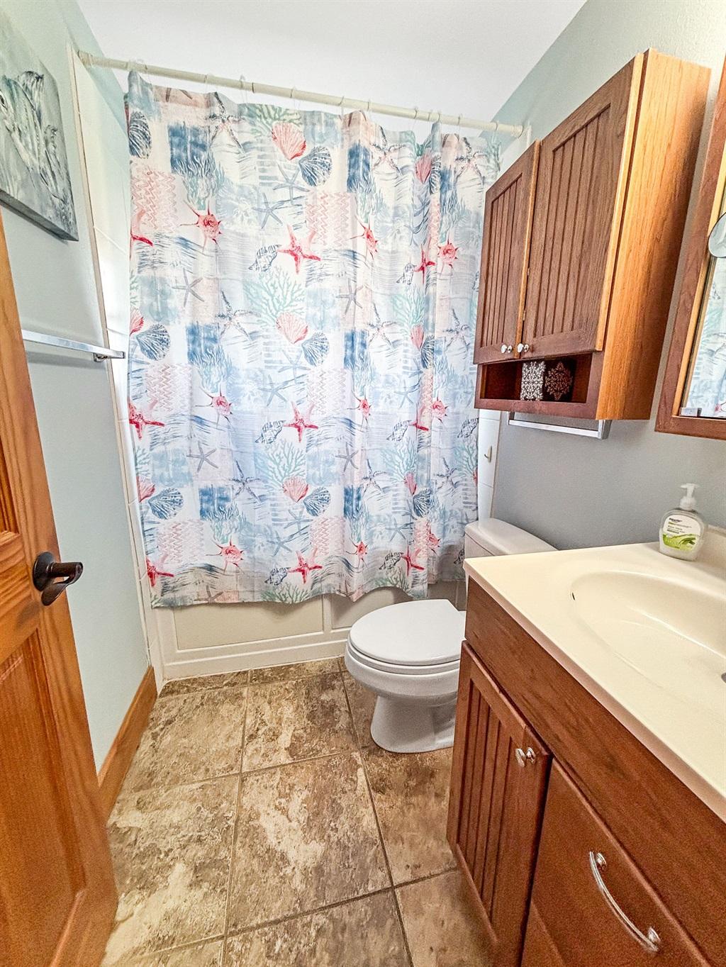 Bathroom with a shower curtain featuring coastal patterns, wooden vanity and cabinet, toilet, and tile flooring.