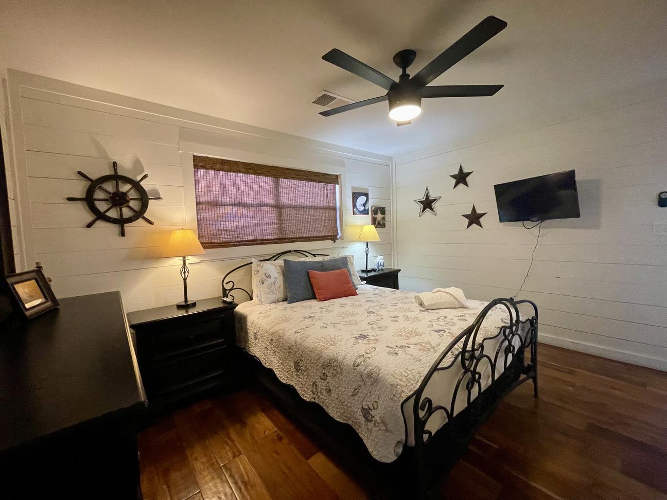 Bedroom with queen bed, coastal decor, and wall-mounted smart TV in Rockport rental