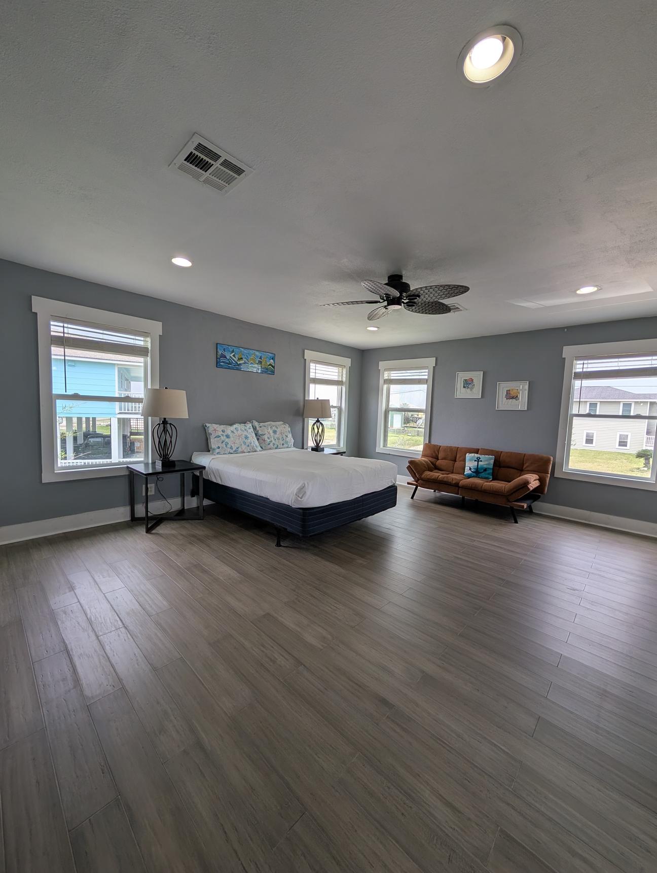 Queen bed in a room with bamboo flooring and windows. 