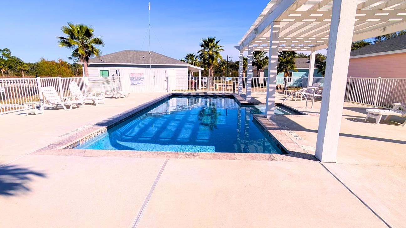 Large community pool with pool house and white pool chairs.