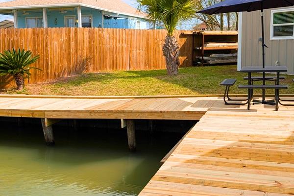Wooden canal dock with water access beside a fenced backyard, featuring a picnic table and grassy yard in Rockport, Texas.