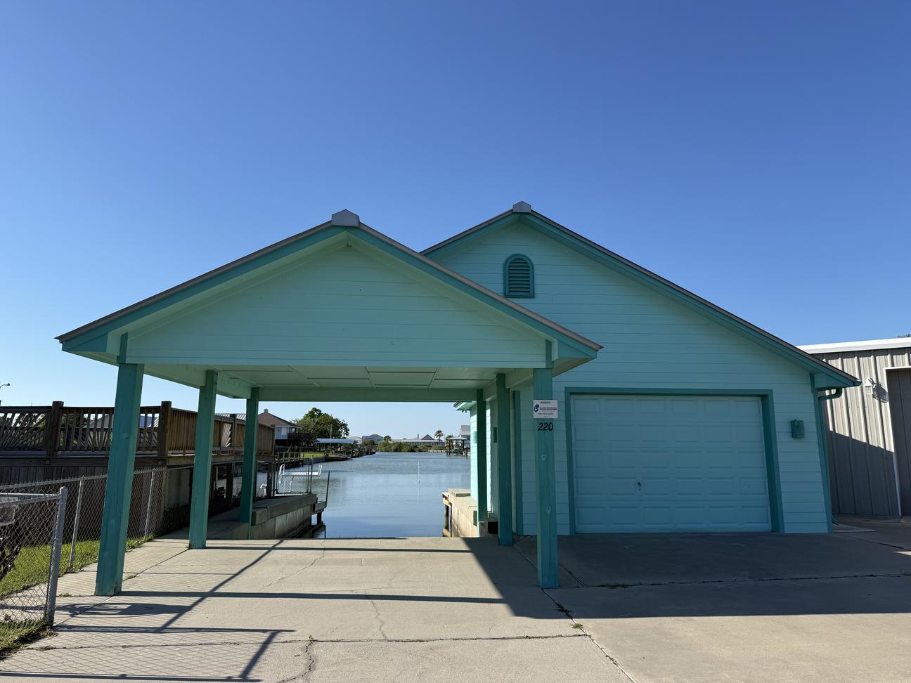 Canal-front coastal home with covered boat parking, garage, private driveway, and direct water access leading out to the bay under a clear blue sky.
