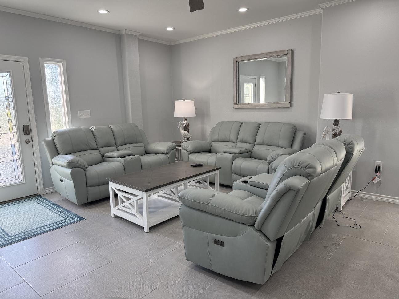 Bright coastal-style living room with plush reclining sofas and chairs, soft neutral décor, modern coffee table, and open seating arrangement in a comfortable vacation rental.