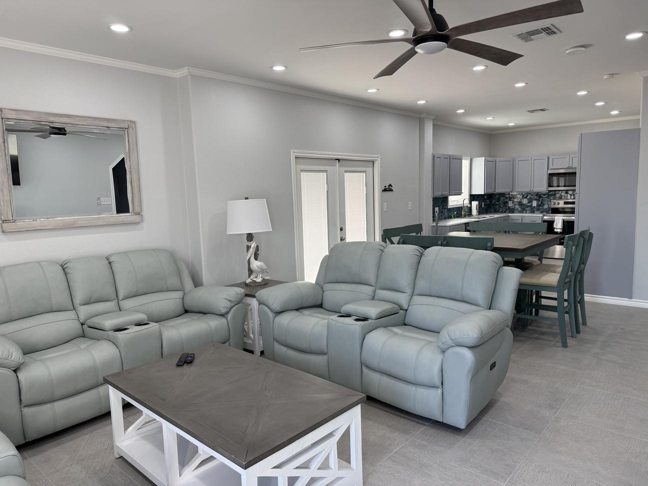 Bright coastal-style living room with plush reclining sofas and chairs, soft neutral décor, modern coffee table, and open seating arrangement in a comfortable vacation rental.