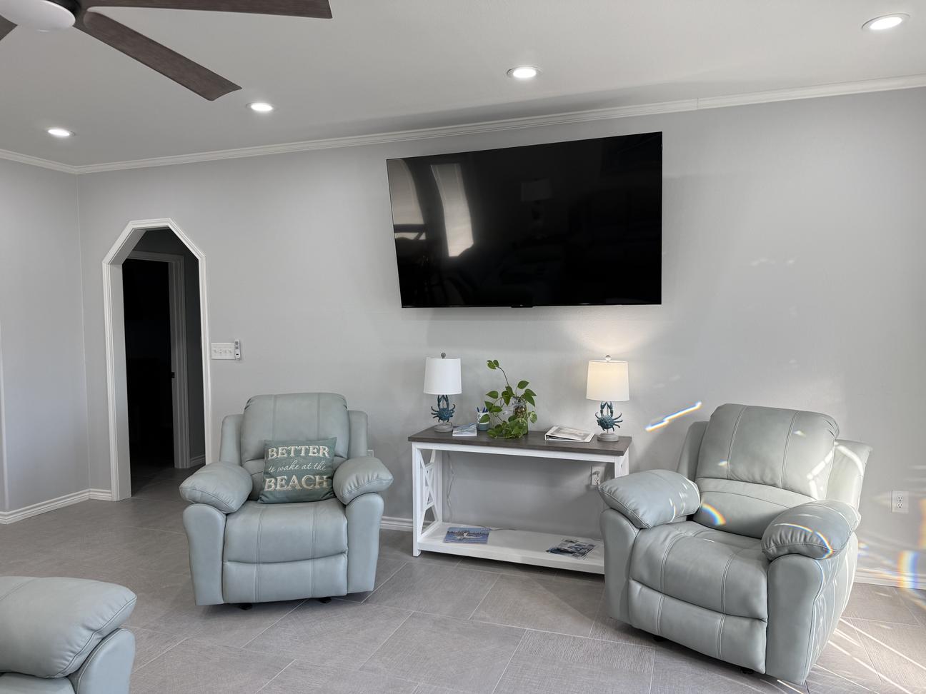 Bright coastal-style living room with plush reclining sofas and chairs, soft neutral décor, modern coffee table, and open seating arrangement in a comfortable vacation rental