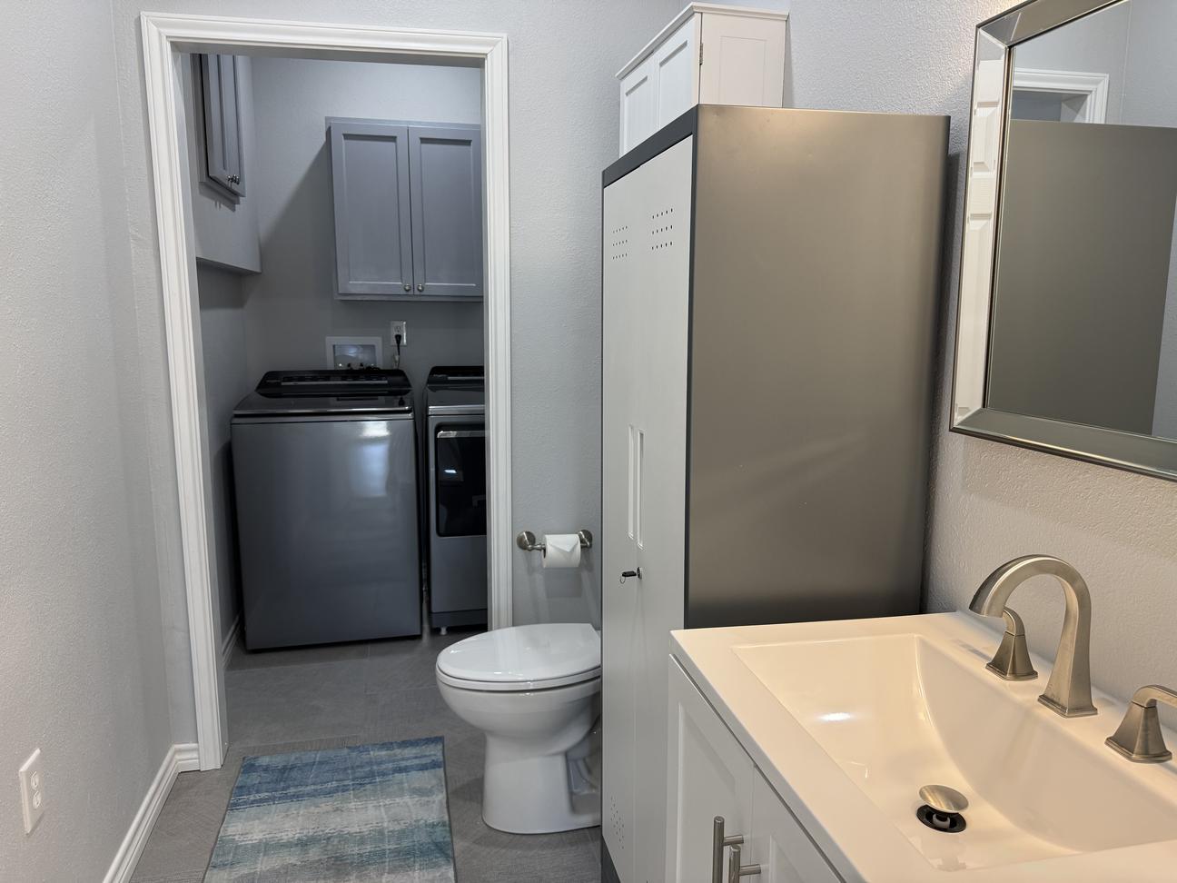 Modern bathroom with walk-in laundry area featuring washer and dryer, white vanity, clean coastal-inspired finishes, and soft neutral décor in a vacation rental.