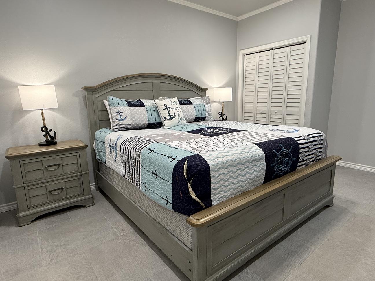 Coastal-inspired bedroom with king bed, nautical-themed bedding, matching nightstands and lamps, shutter-style closet doors, and soft neutral décor in a spacious vacation rental.