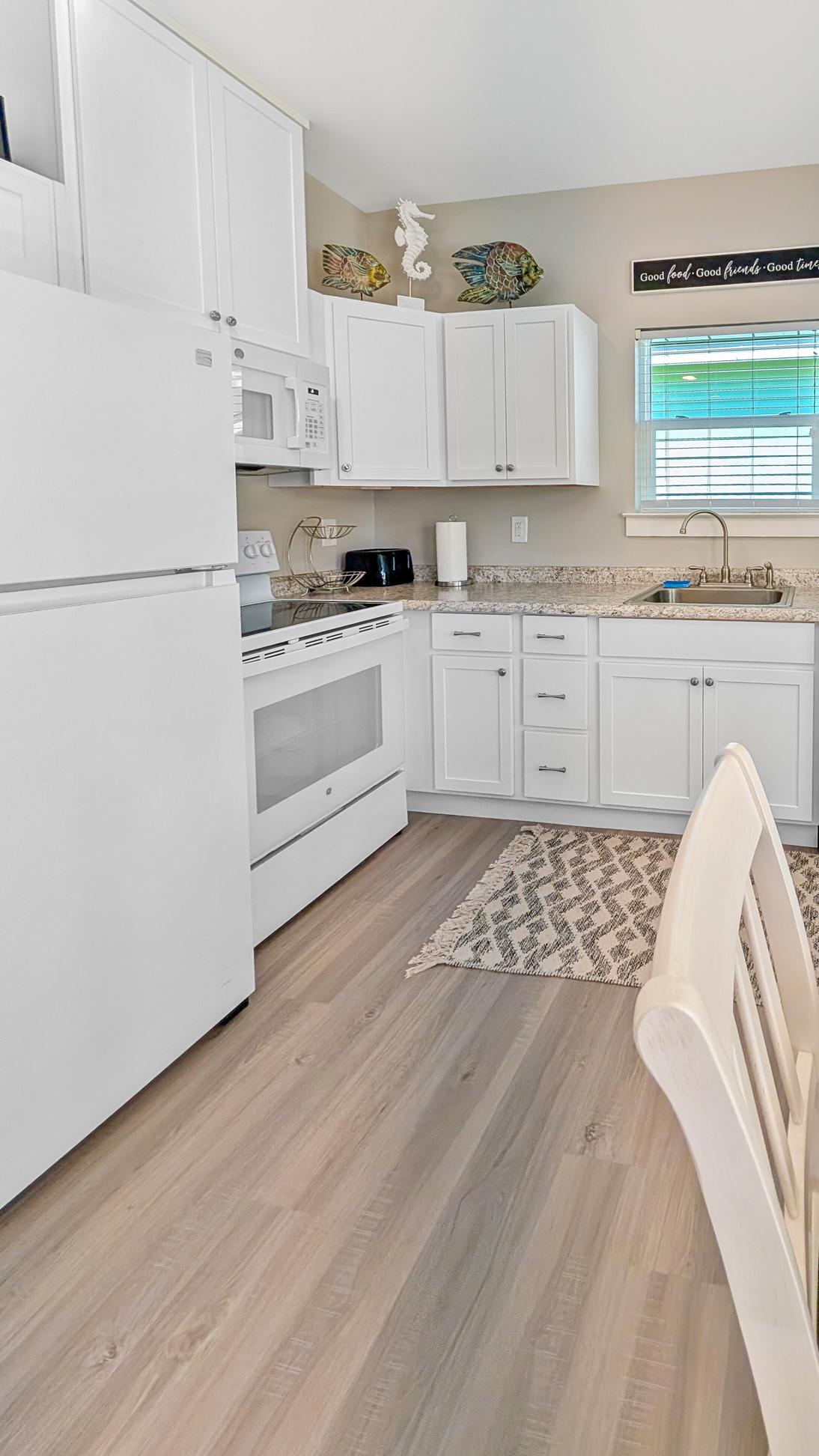 Light wood floors in an open concept kitchen with white appliances and white cupboards. 