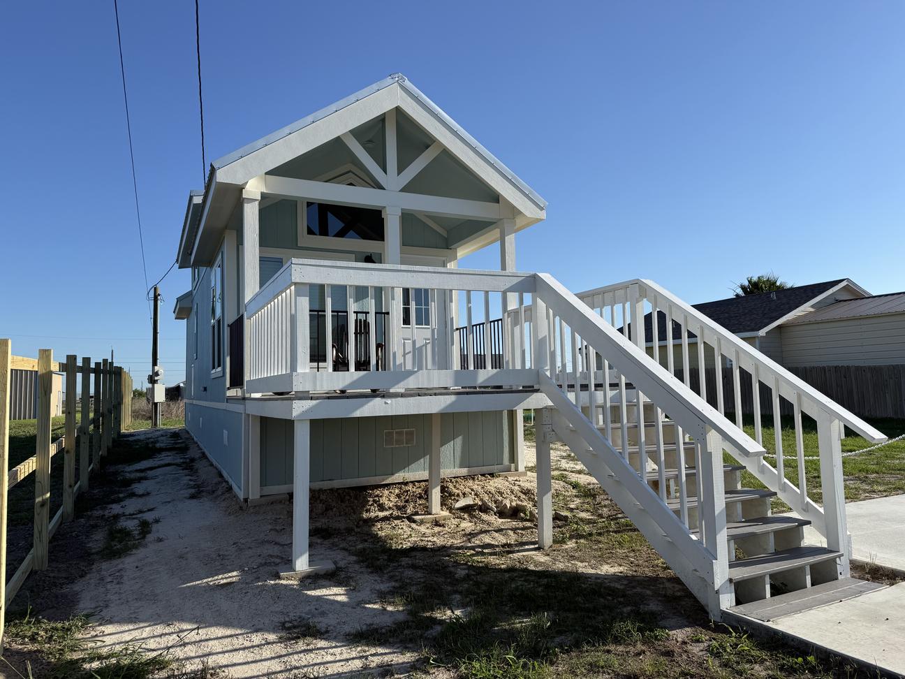 Blue and white tiny home with a large porch and stairs.