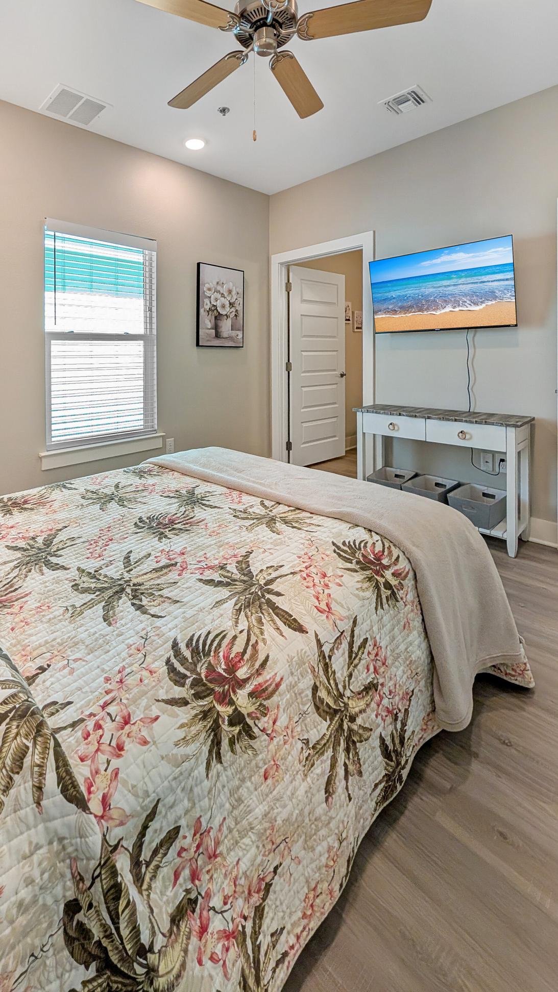 Queen sized bed in a bedroom decorated in blue and tan tones, with private bath and smart tv.