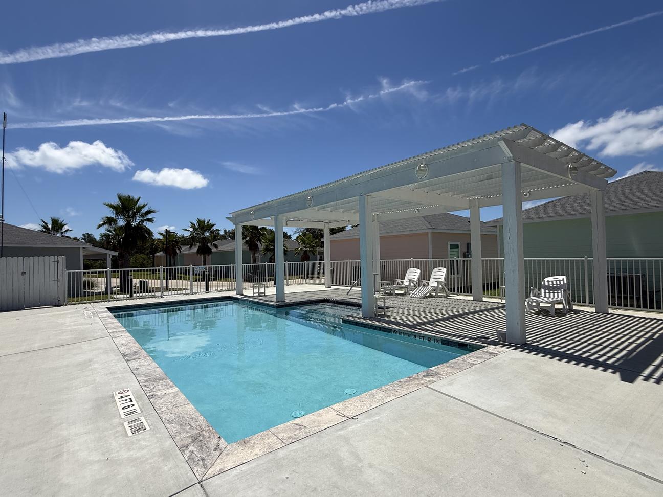Blue swimming pool with white pool furniture and shade. 