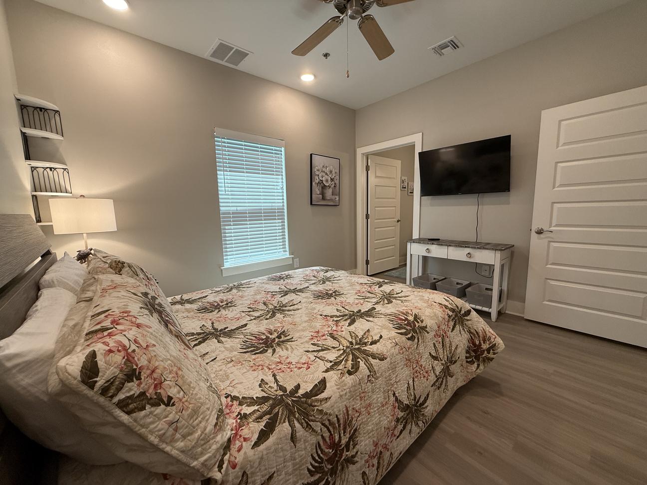 Tan and brown tropical bedding on a queen bed with smart tv on the wall. 