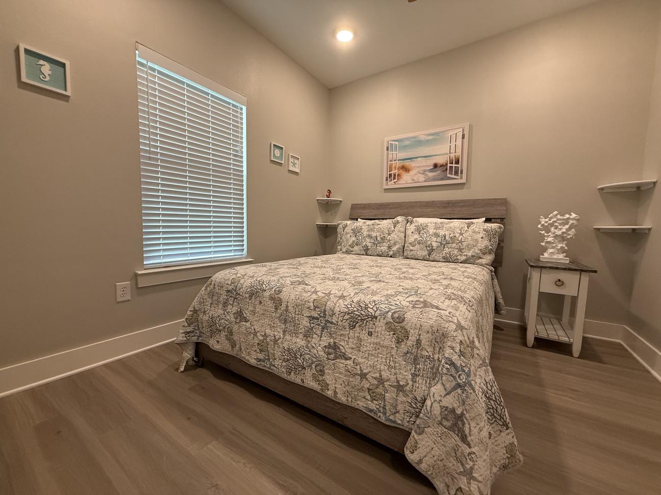 Queen bed with coastal themed decor in a bright room. 