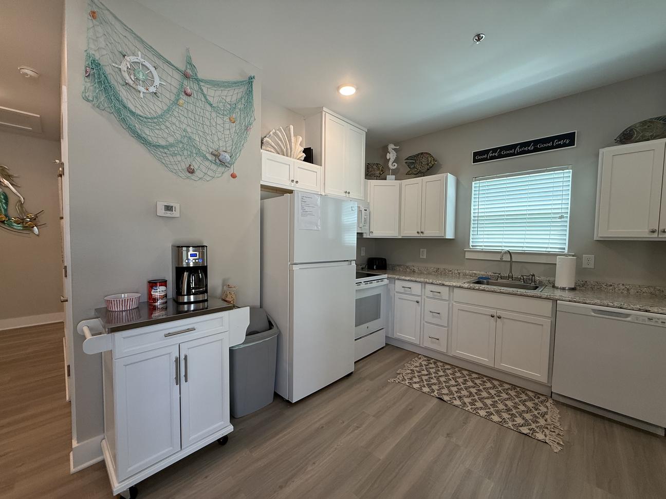 Coastal-inspired vacation rental interior with wood accent TV wall, beach-themed décor, coffee station, hallway leading to bedrooms, and light modern finishes throughout the space.