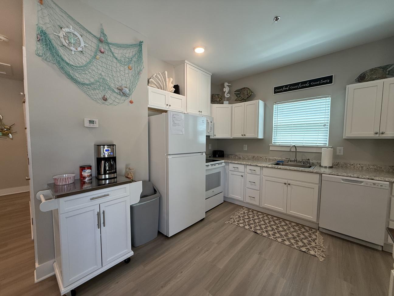 Bright coastal-style kitchen with white cabinetry, full-size appliances, coffee station, beach-inspired décor, and open floor plan in a modern vacation rental.