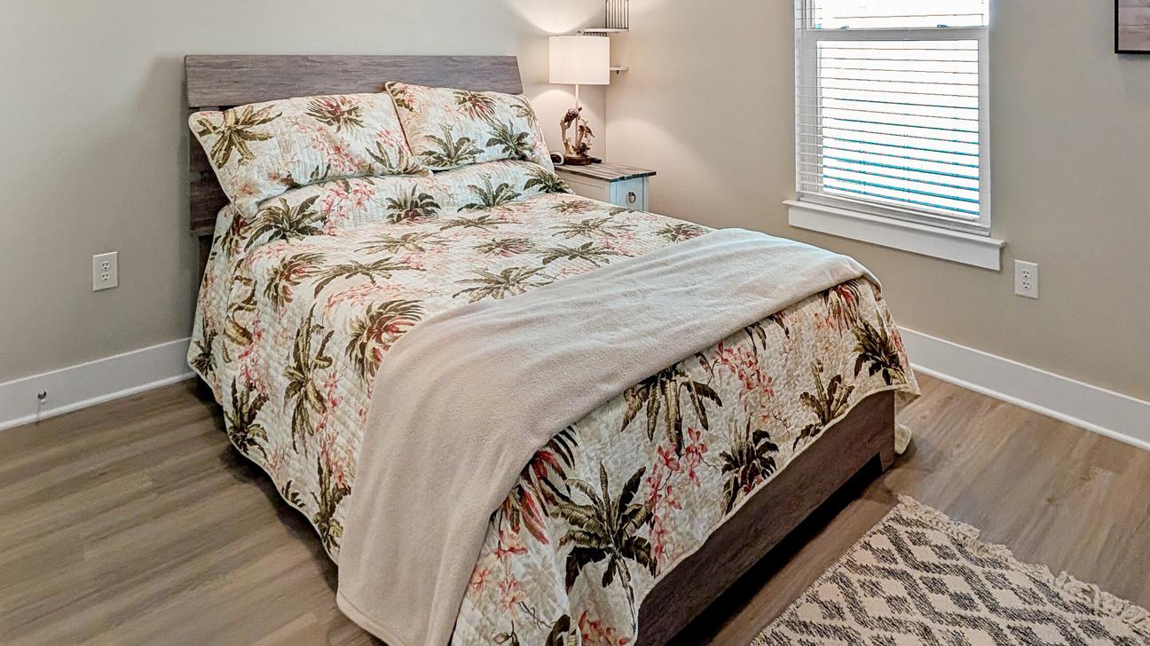 Tan coastal bedding featuring palm trees on the queen bed with a window