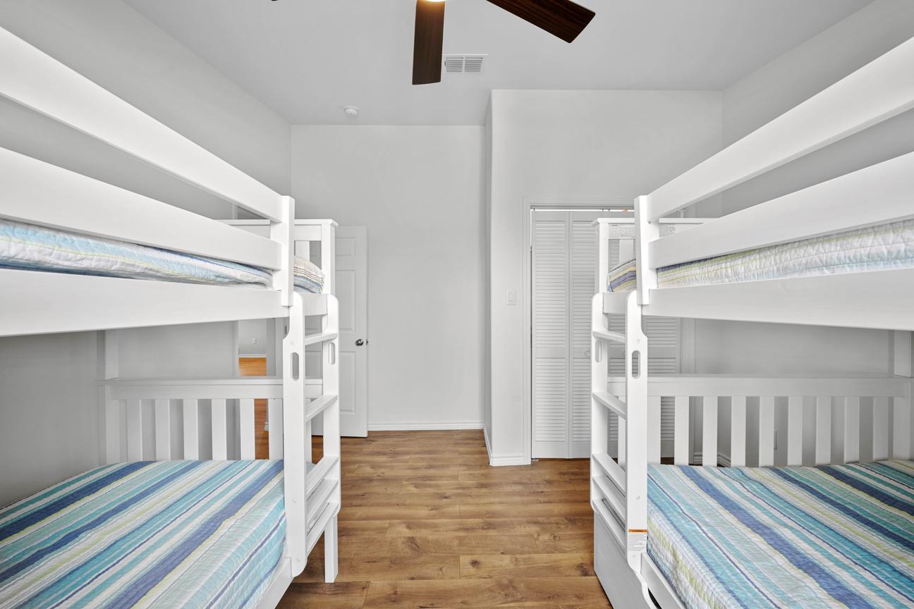 Spacious bedroom with two white bunk beds, blue striped bedding, wood-look floors, and a ceiling fan.