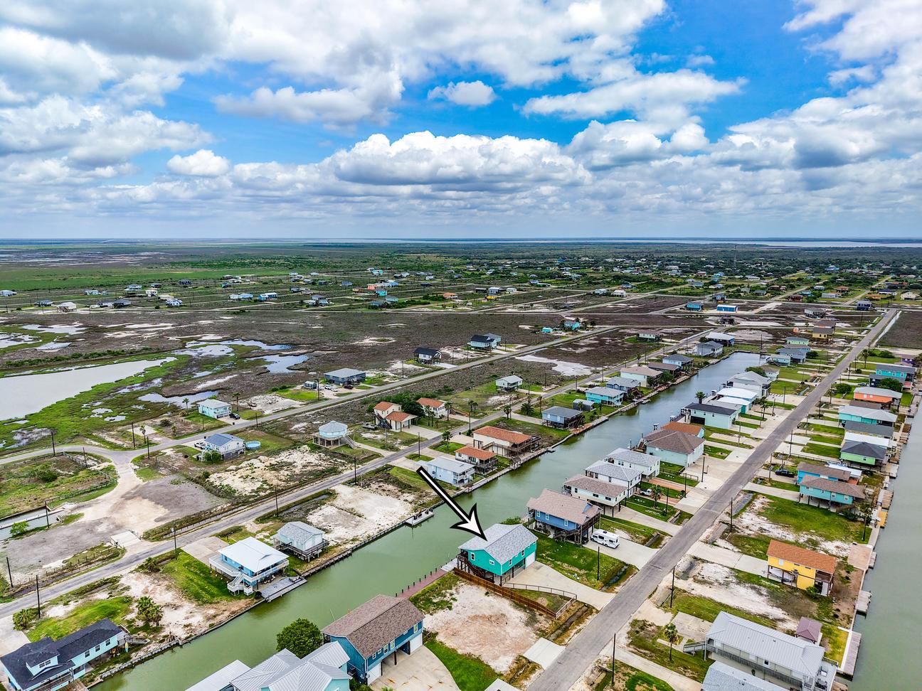 Aerial view of a Rockport canal neighborhood with an arrow marking a turquoise waterfront vacation home.