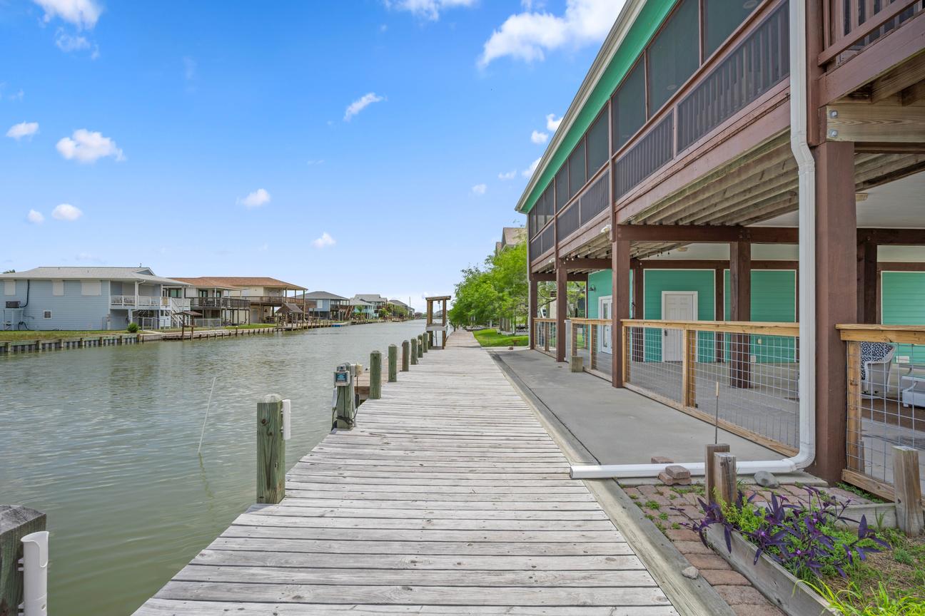 Long private wooden dock beside a turquoise canal-front home, with calm water and neighboring coastal houses.