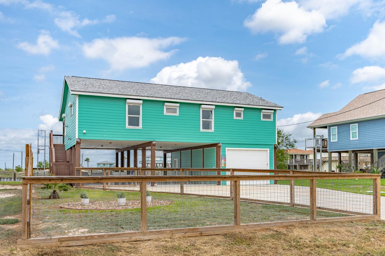 Turquoise coastal vacation home with a fully fenced yard, covered patio, and gated driveway.