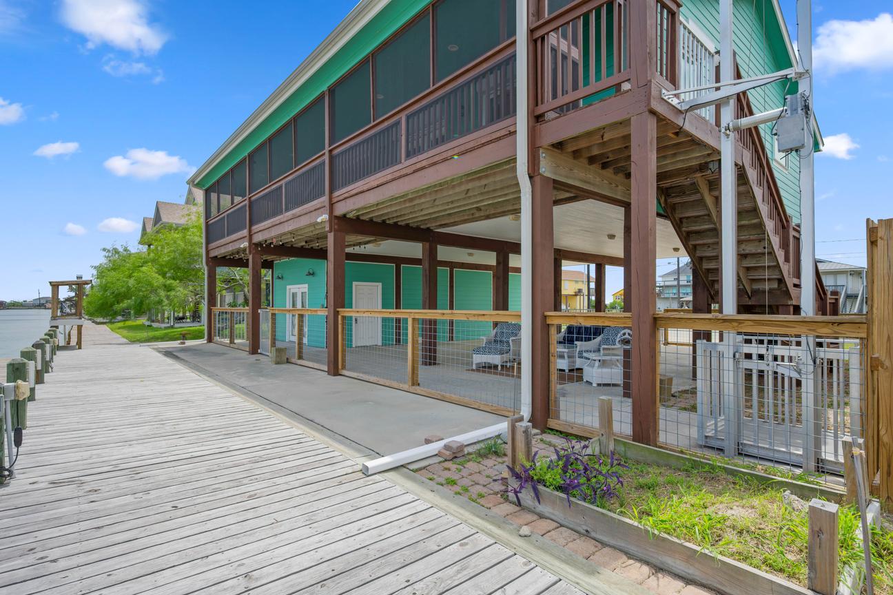 Canal-side home with an upper screened deck, covered ground-level patio, fenced outdoor area, and private wooden dock.