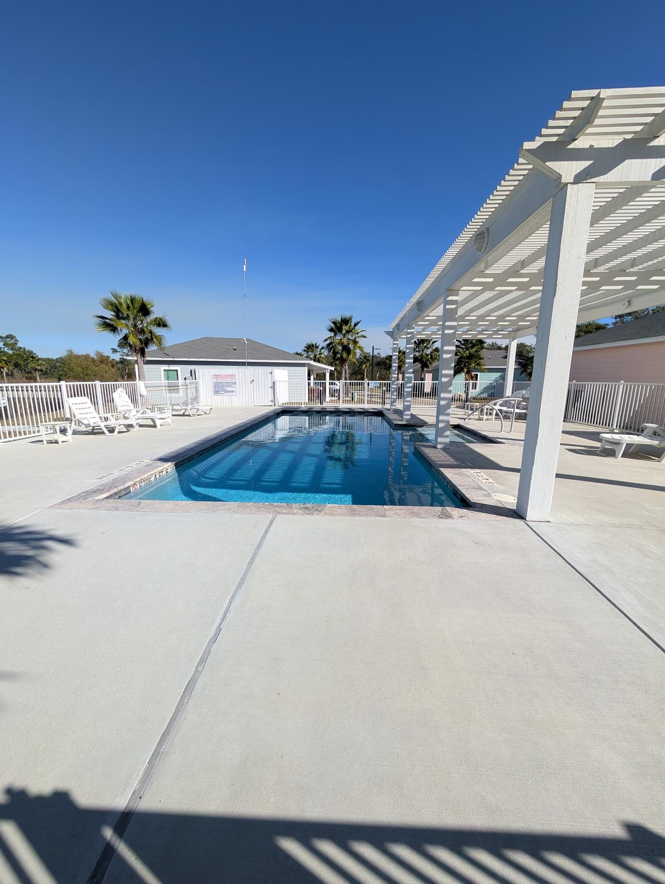 Blue swimming pool with white pool furniture and shade. 