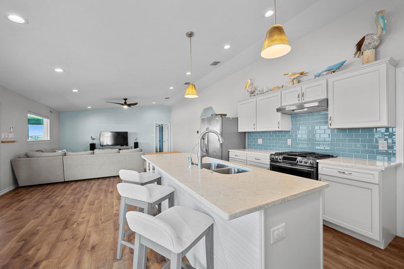Bright coastal kitchen at SeaGlass Smiles with a large island, three barstools, white cabinetry, and a blue tile backsplash.