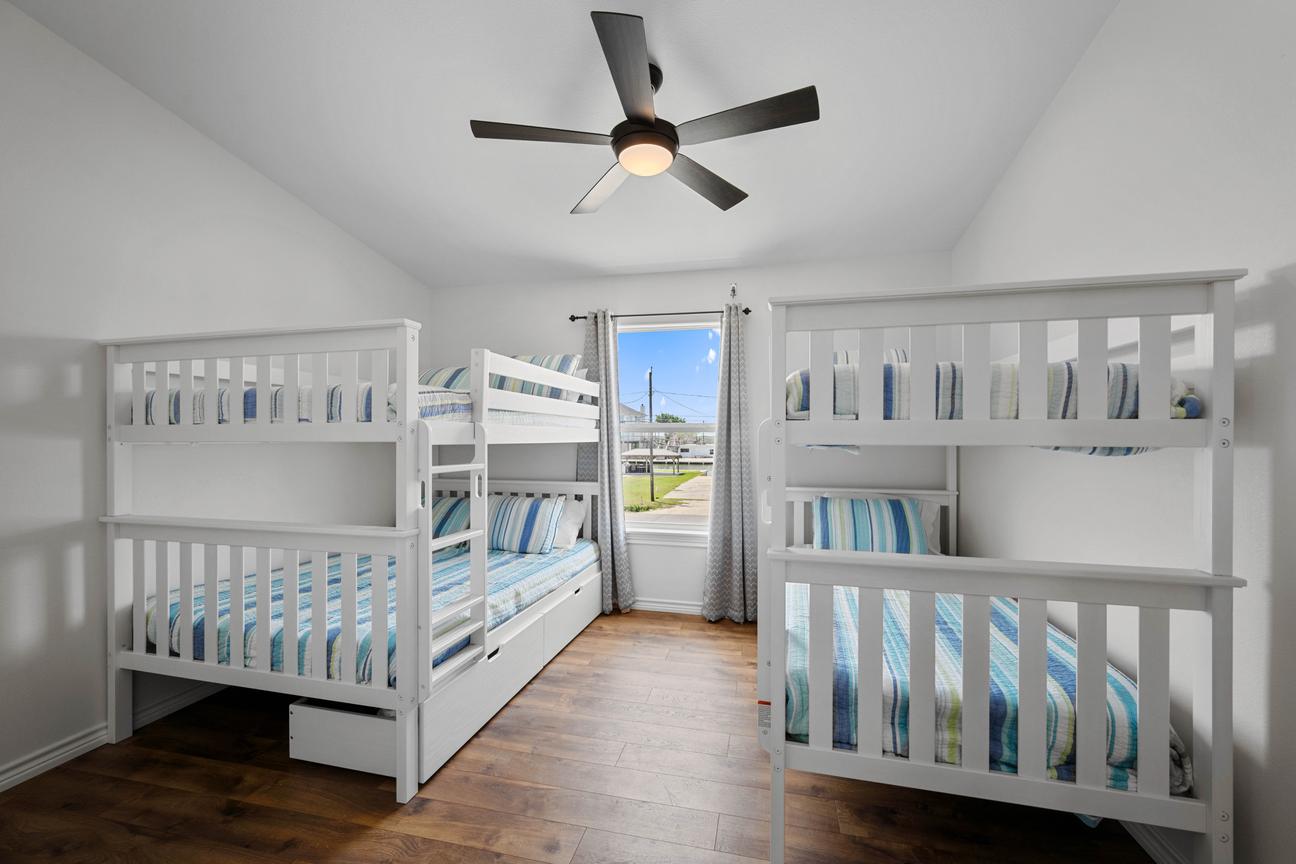 Bright coastal bunk room with one queen-over-queen bunk bed, one twin-over-twin bunk bed, blue striped bedding, and a ceiling fan.