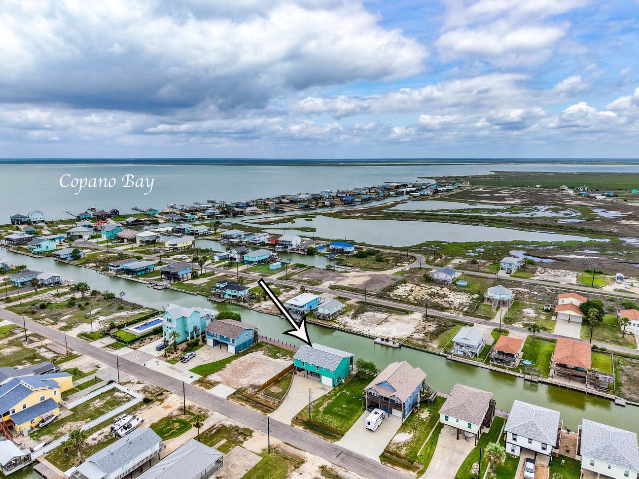 Aerial view of a canal-front neighborhood beside Copano Bay, with an arrow marking the waterfront vacation rental.