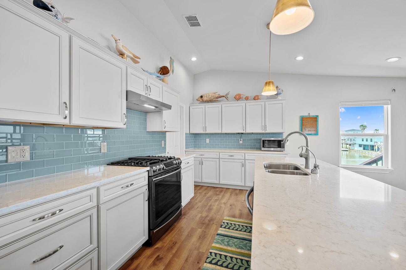 Bright kitchen with white cabinetry, a sea-blue tile backsplash, black gas range, and large island with a double sink.