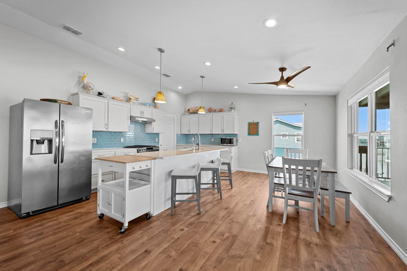 Open kitchen and dining area with white cabinetry, stainless steel appliances, island seating, and a table for six.