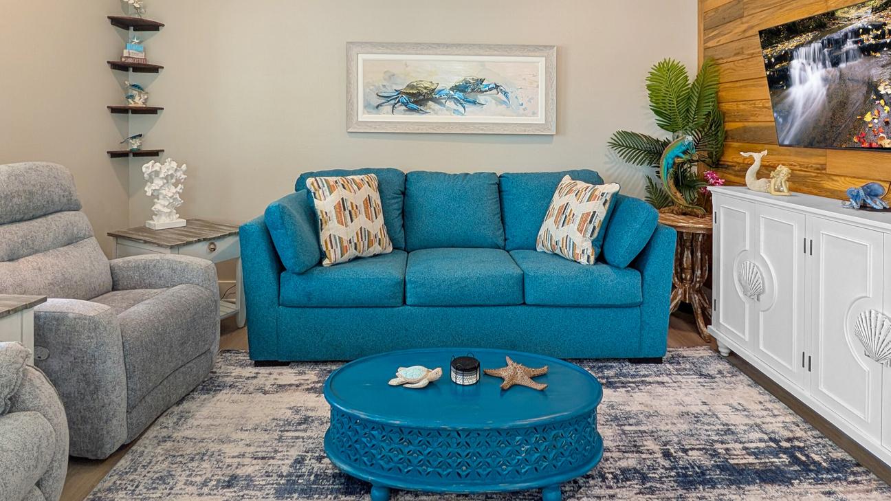Living room with a blue sofa, recliner, round coffee table with coastal decor, wall art of crabs, and a TV on a cabinet with wood accent wall.