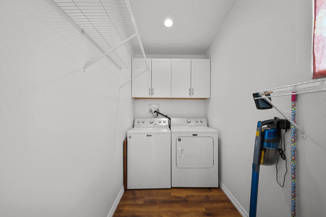 Laundry room with a full-size washer and dryer, overhead cabinets, wire shelving, and hanging space.