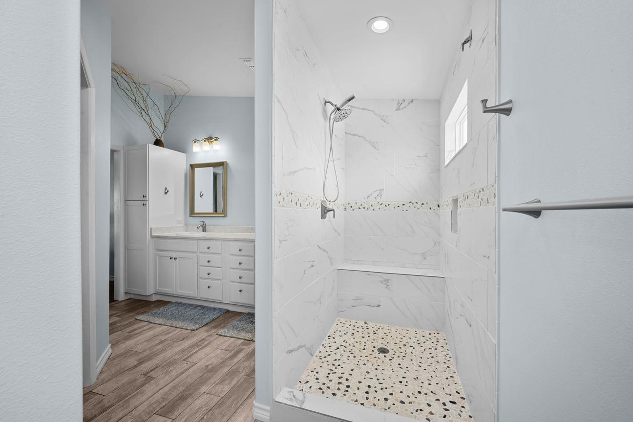 Primary bathroom with a spacious walk-in shower, marble-look tile, pebble-style floor, and built-in bench.