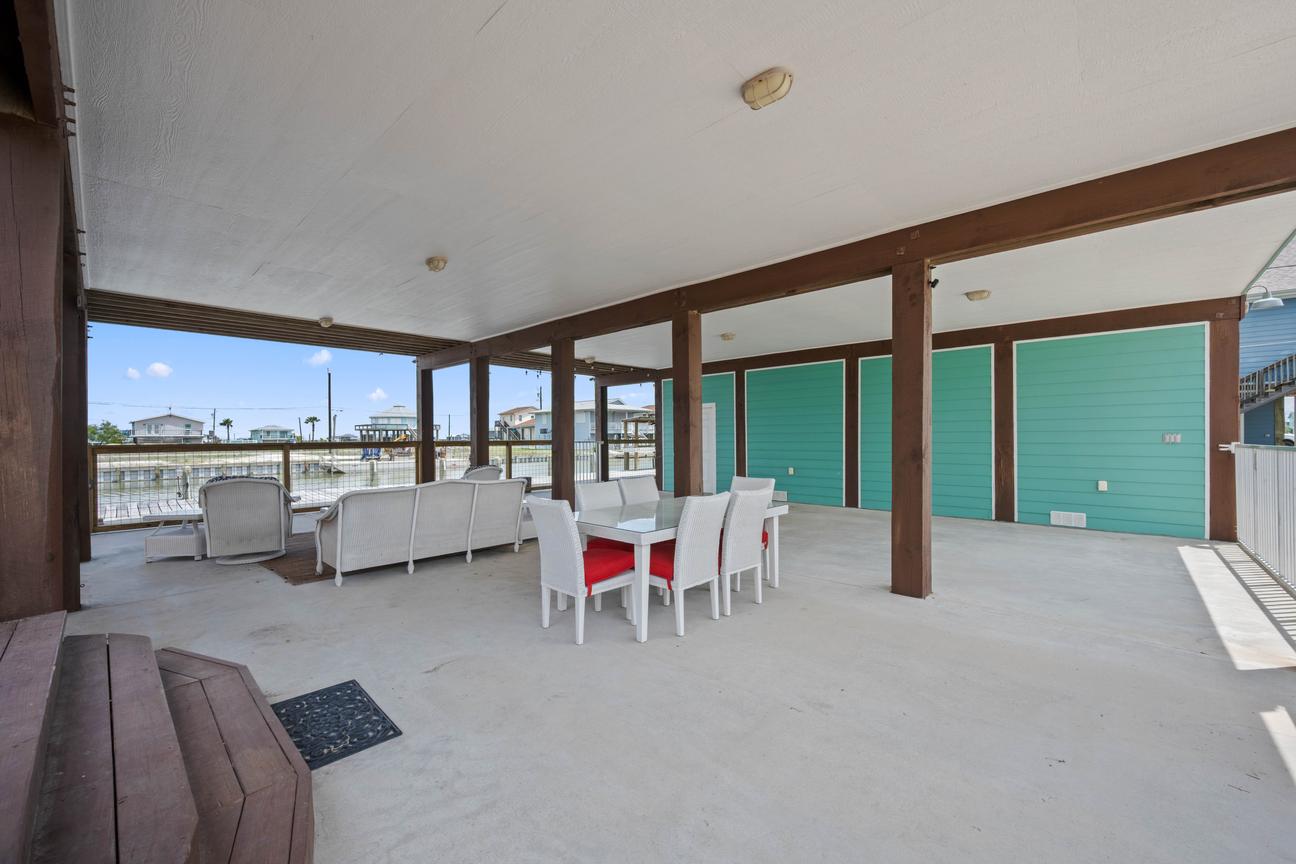 Covered waterfront patio with a dining table, cushioned lounge seating, turquoise walls, and canal views.