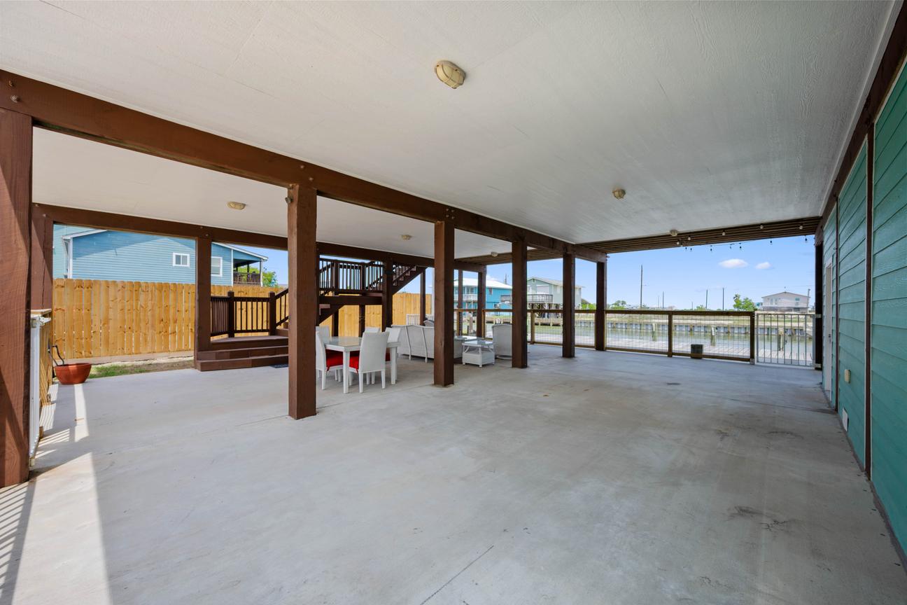 Large covered waterfront patio with an outdoor dining table, string lights, fenced yard, and canal views.