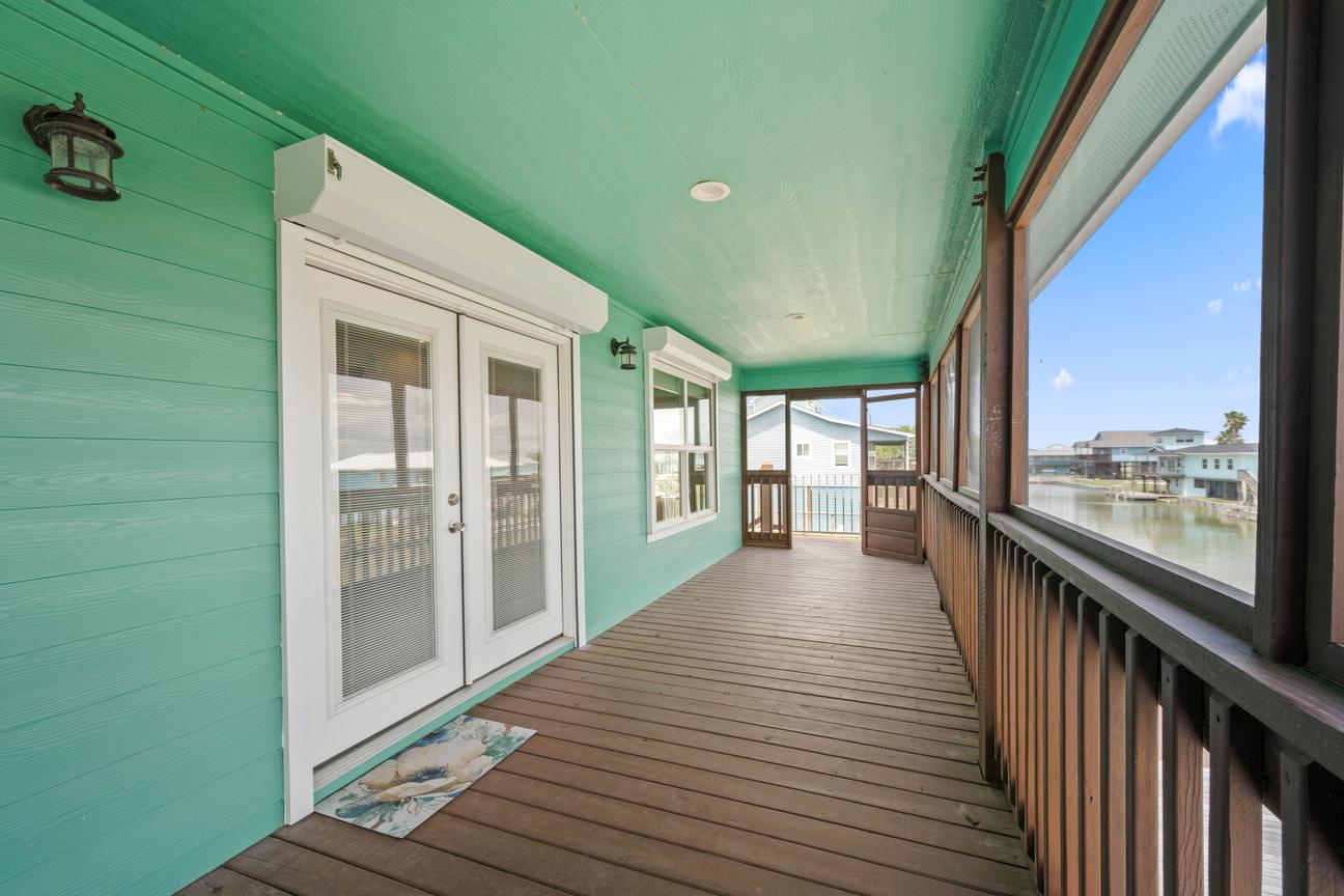 Spacious screened deck with turquoise walls, wood flooring, French doors, and views of the canal.