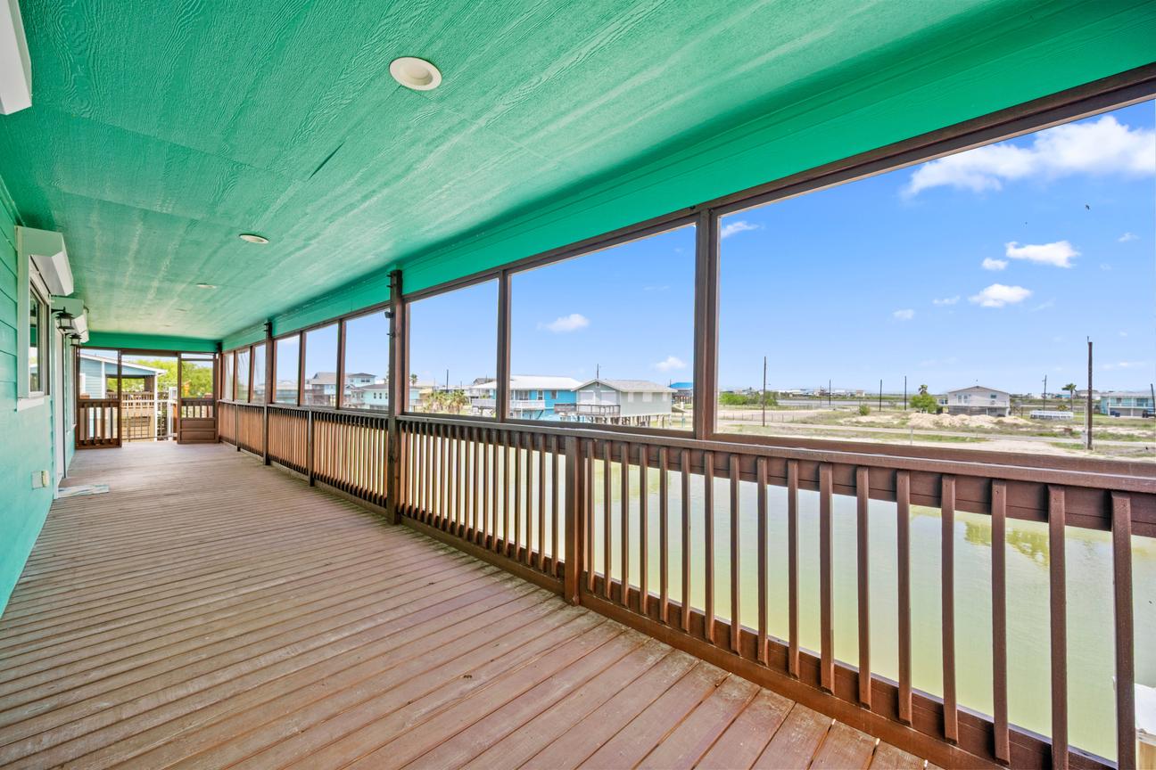 Long screened waterfront deck with wood flooring, turquoise ceiling, railing, and panoramic canal views.