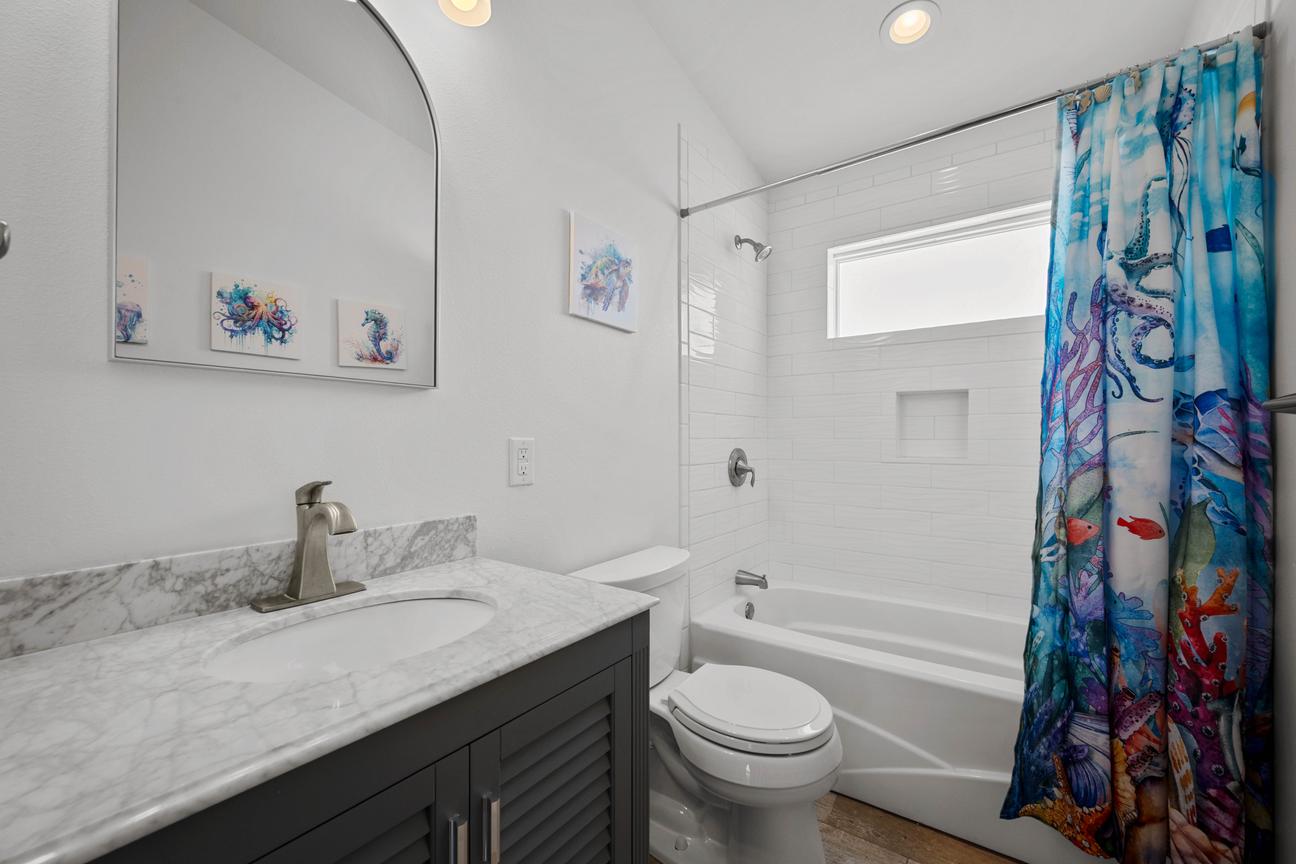 Shared bathroom with a gray vanity, full tub-and-shower combination, built-in wall niche, and marine-life shower curtain.